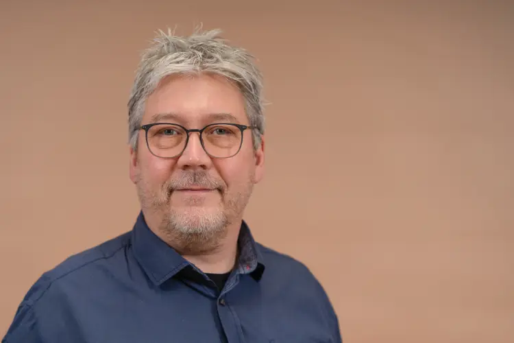 Porträtaufnahme: Mann mit grauen Haaren, grauem Vollbart und Brille schaut in die Kamera
