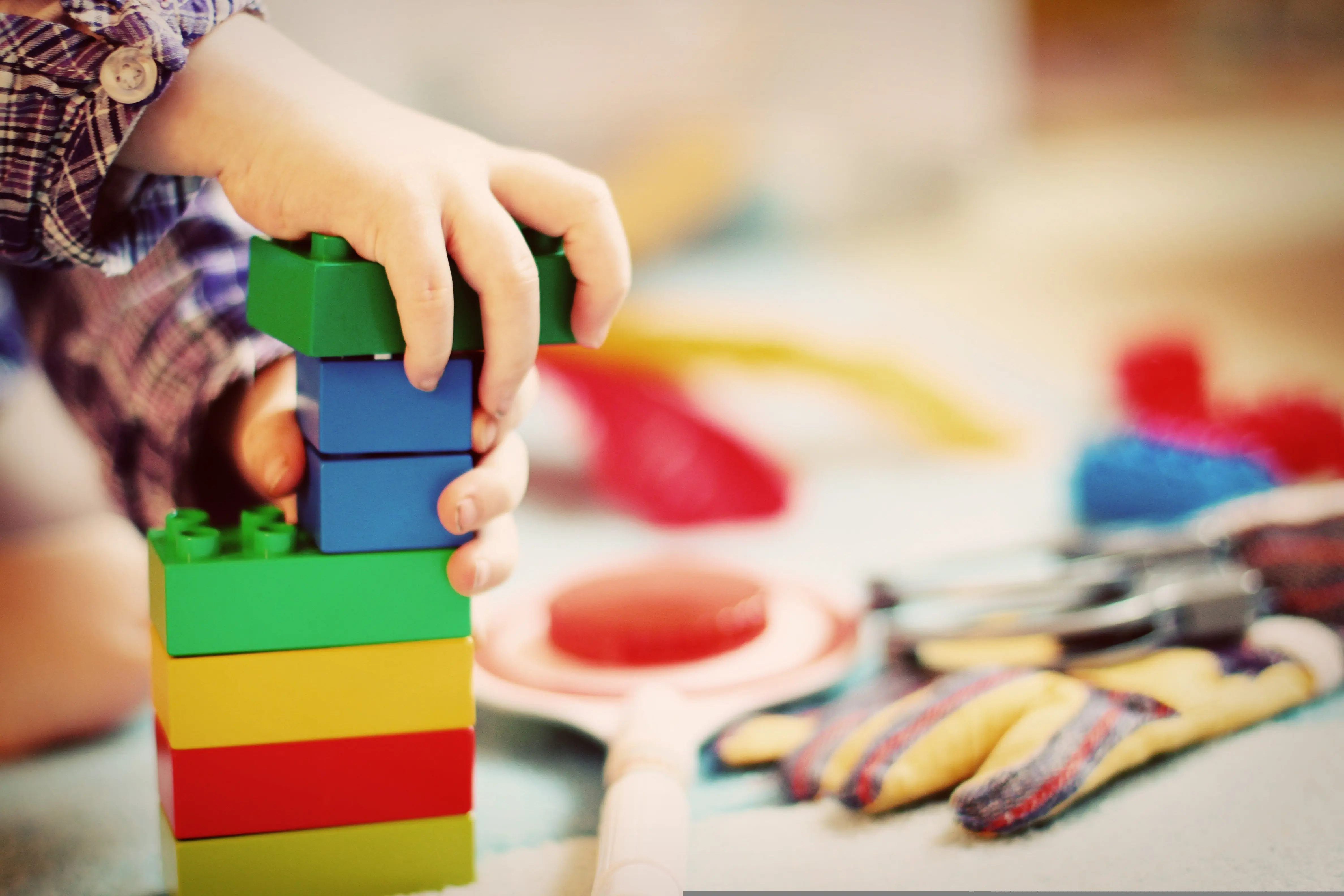 Kinderhände bauen einen Turm aus bunten Spielsteinen.