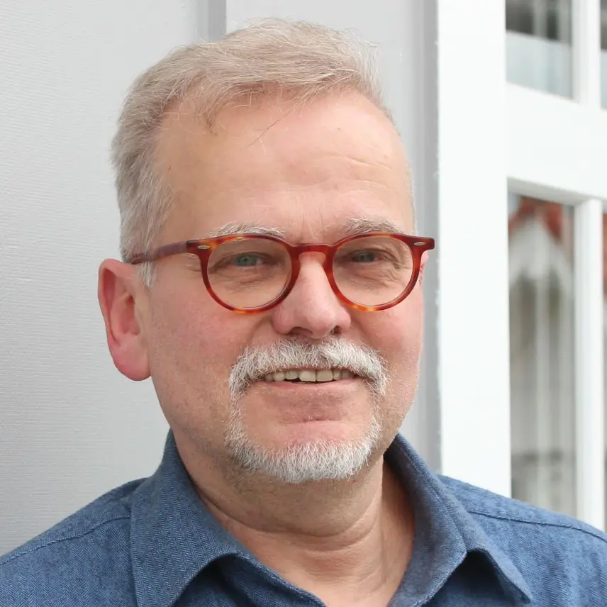 Kopfporträt von Mann mit grauem Haar und roter Brille