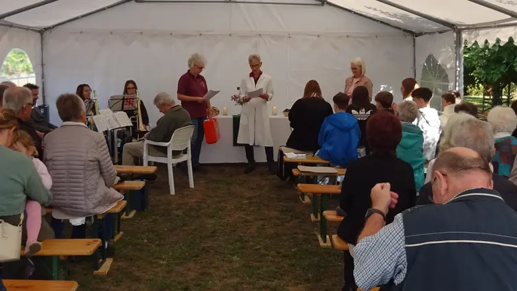 Das Foto zeigt die Besuchenden, drei Mitwirkende und die Mitglieder des Breuberger Posaunenchors im Gottesdienst im Festzelt am Kohlplatz in Breuberg-Hainstadt.