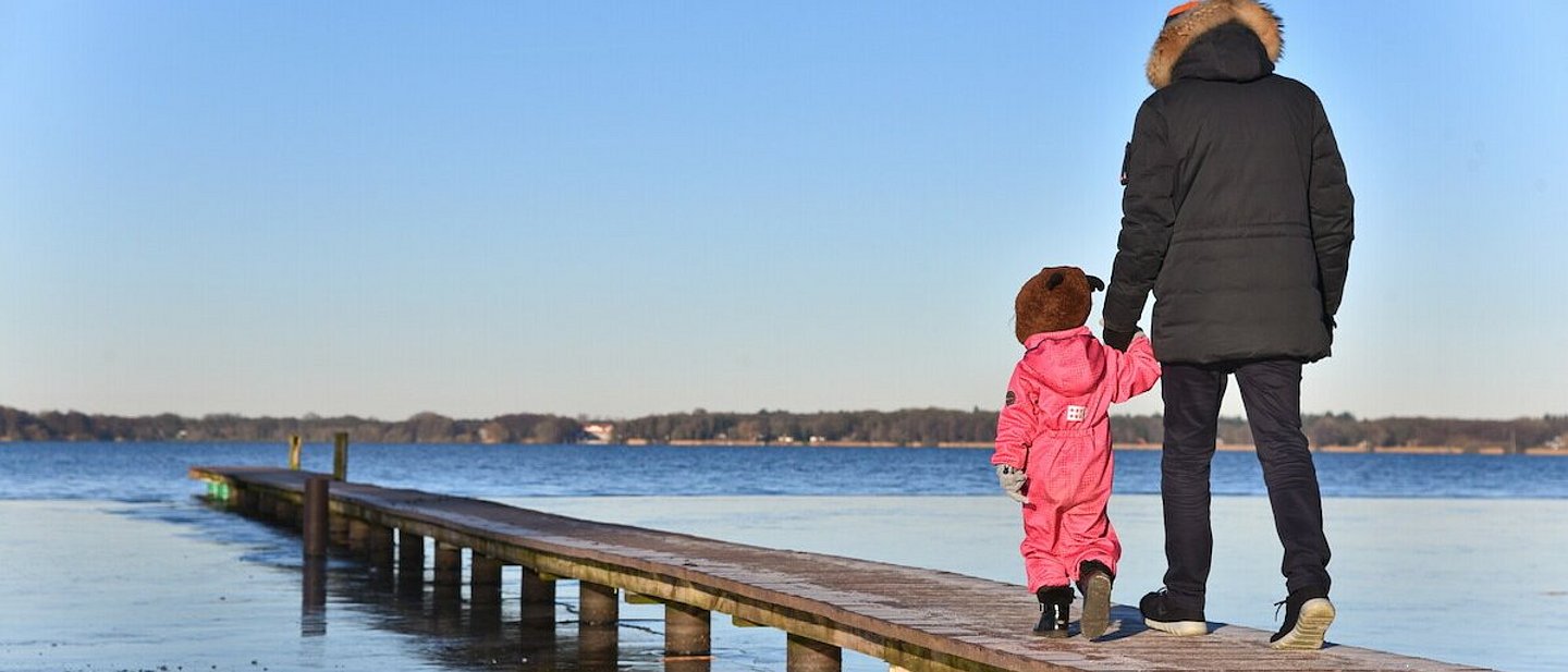 Ein Vater mit seinem Kind Hand in Hand auf einem Steg über Wasser