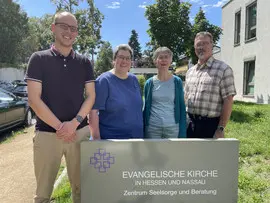 Vier Personen stehen vor dem Schild der Evangelischen Kirche in Hessen und Nassau in Darmstadt: von links Julian Gick, Lydia Ploch, Dorothea Hillingshäuser und Dr. Gerald Schwalbach.