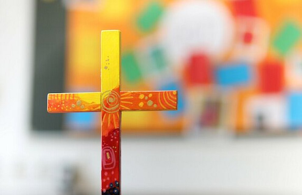 buntes Holzkreuz auf Tuch auf einem Tisch.