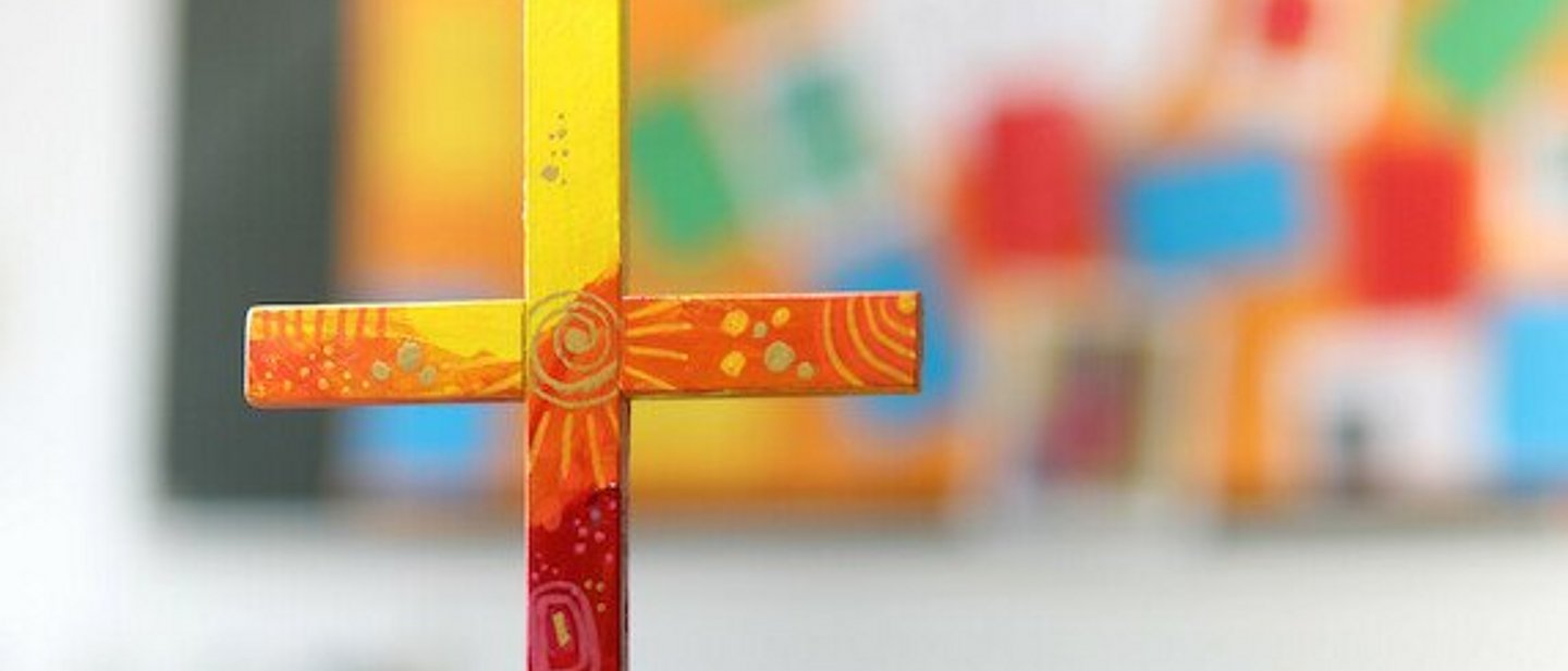 buntes Holzkreuz auf Tuch auf einem Tisch.