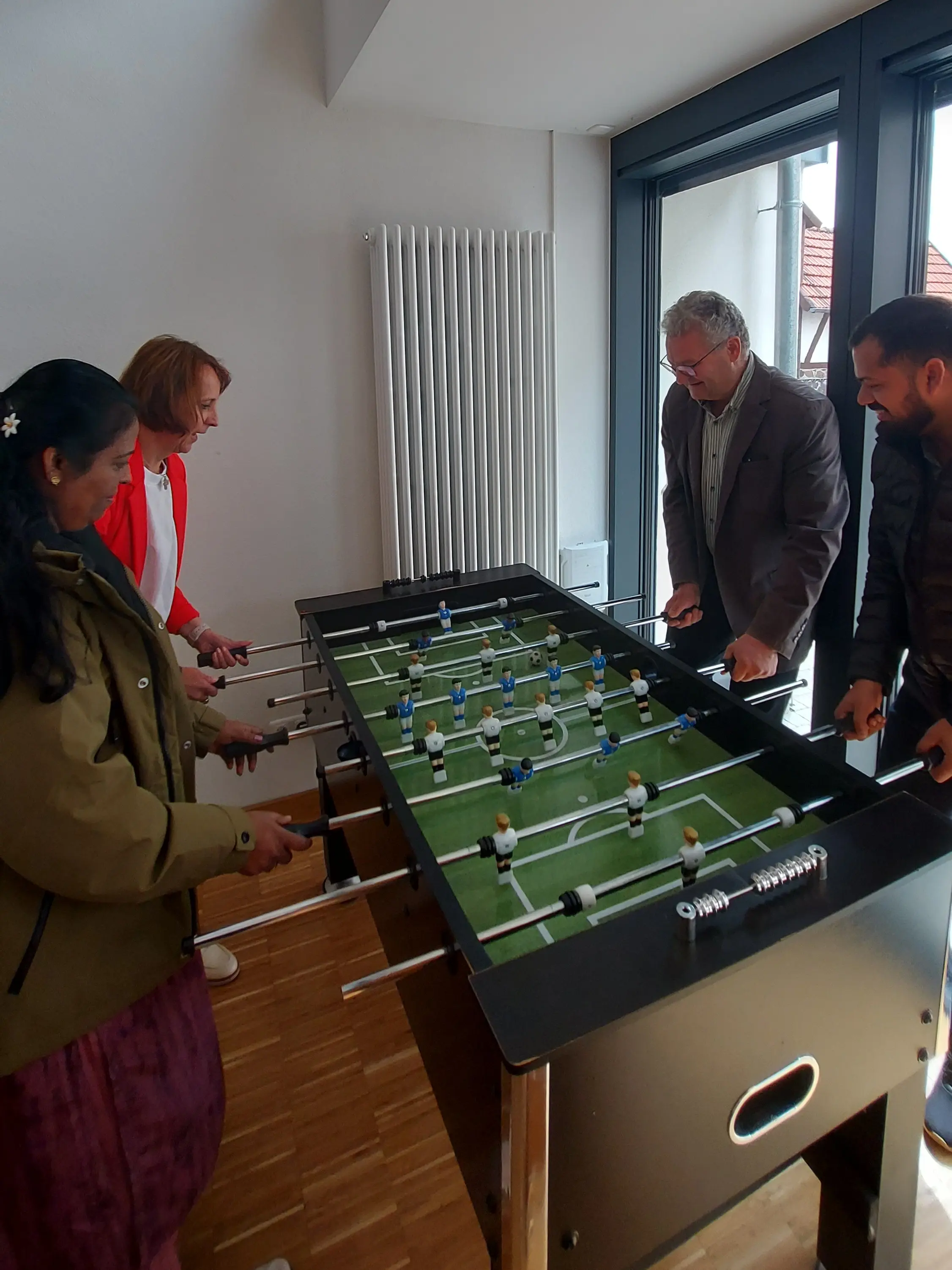 Tischkicker, links zwei Frauen, rechts zwei Männer, spielen Tischfußball,