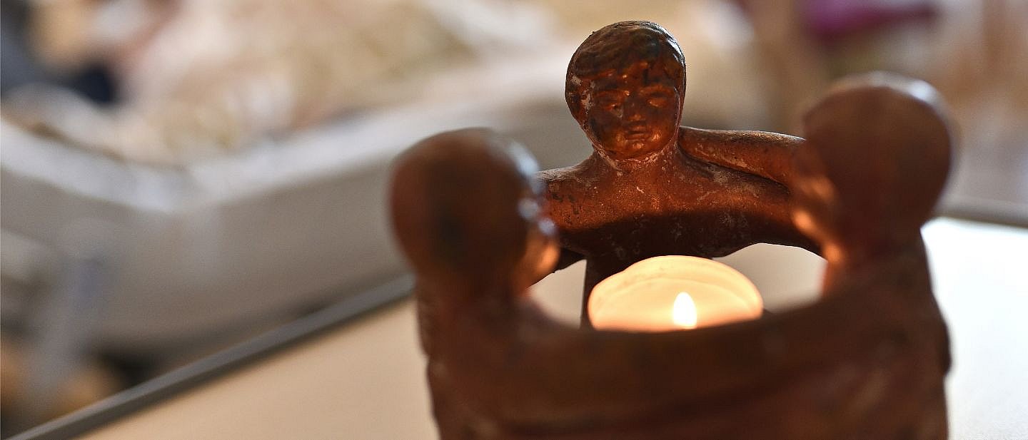 ein Teelichhalter mit Kindern aus Ton und einem brennenden Teelicht