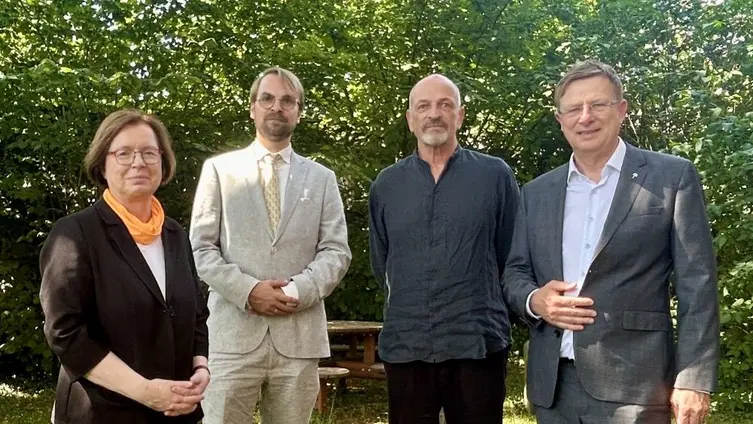 Die vier genannten Personen stehen auf einer Wiese schauen in die Kamera 