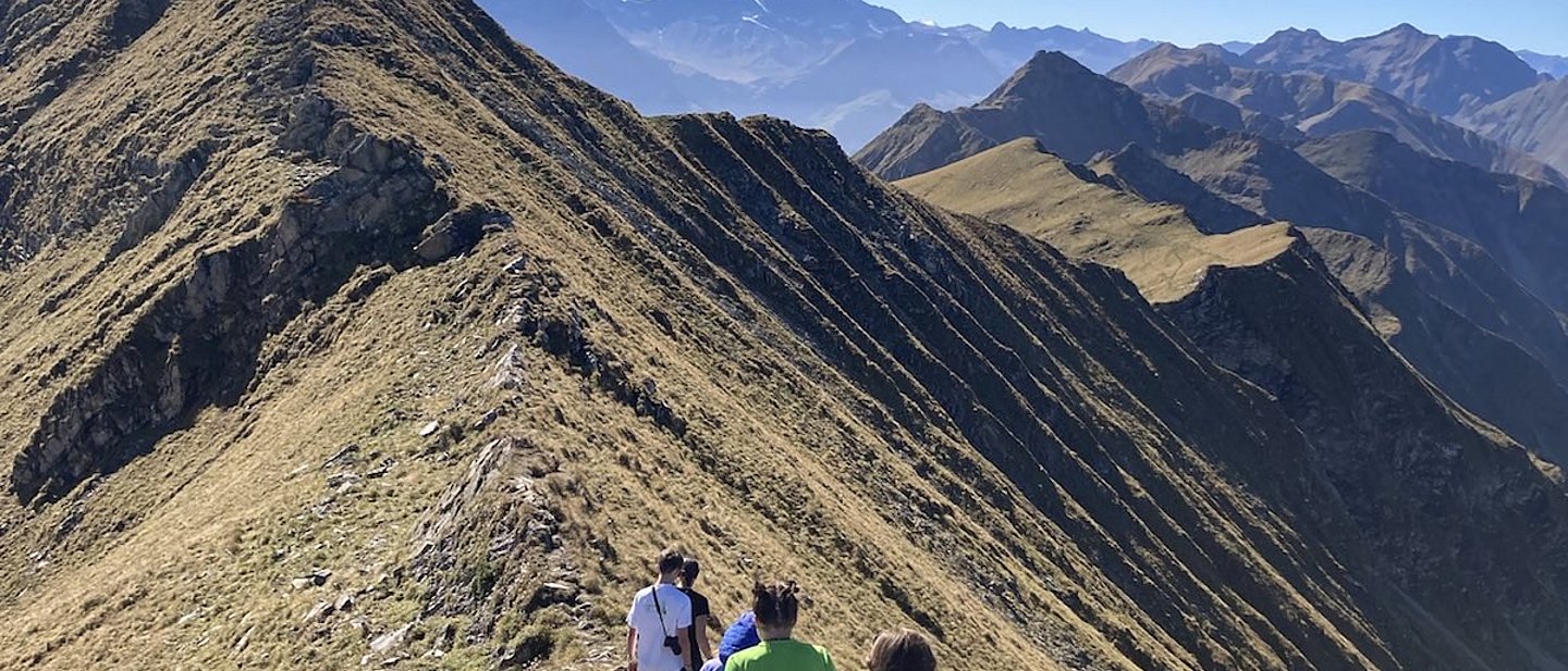 Jugendliche wandern auf einem Grat hintereunander. Blauer Himmel ist zu sehen und einen Berggrat.