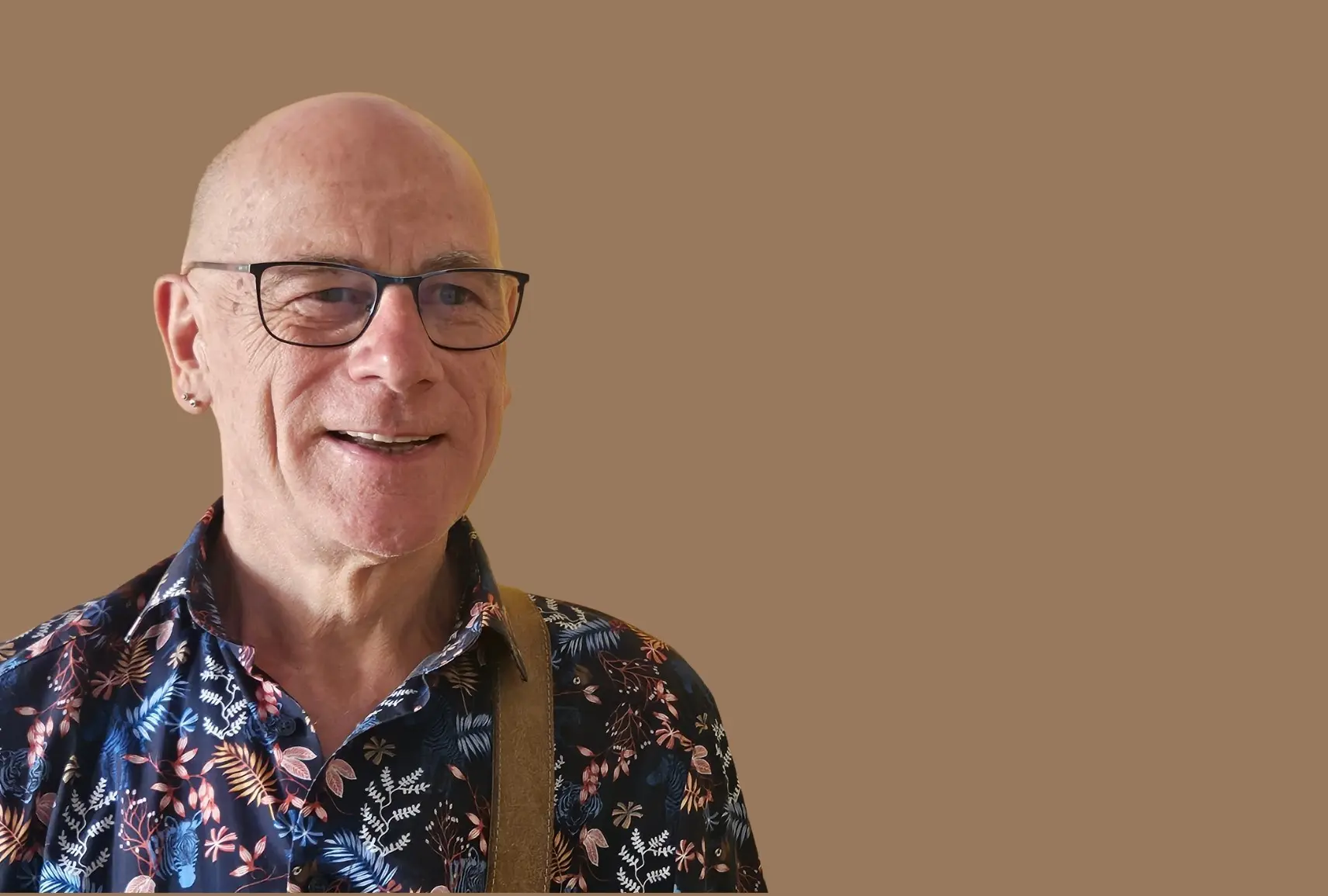 Wilfried Schutt, kahler Kopf, Ohrring, Brille, lächelt in die Kamera. 