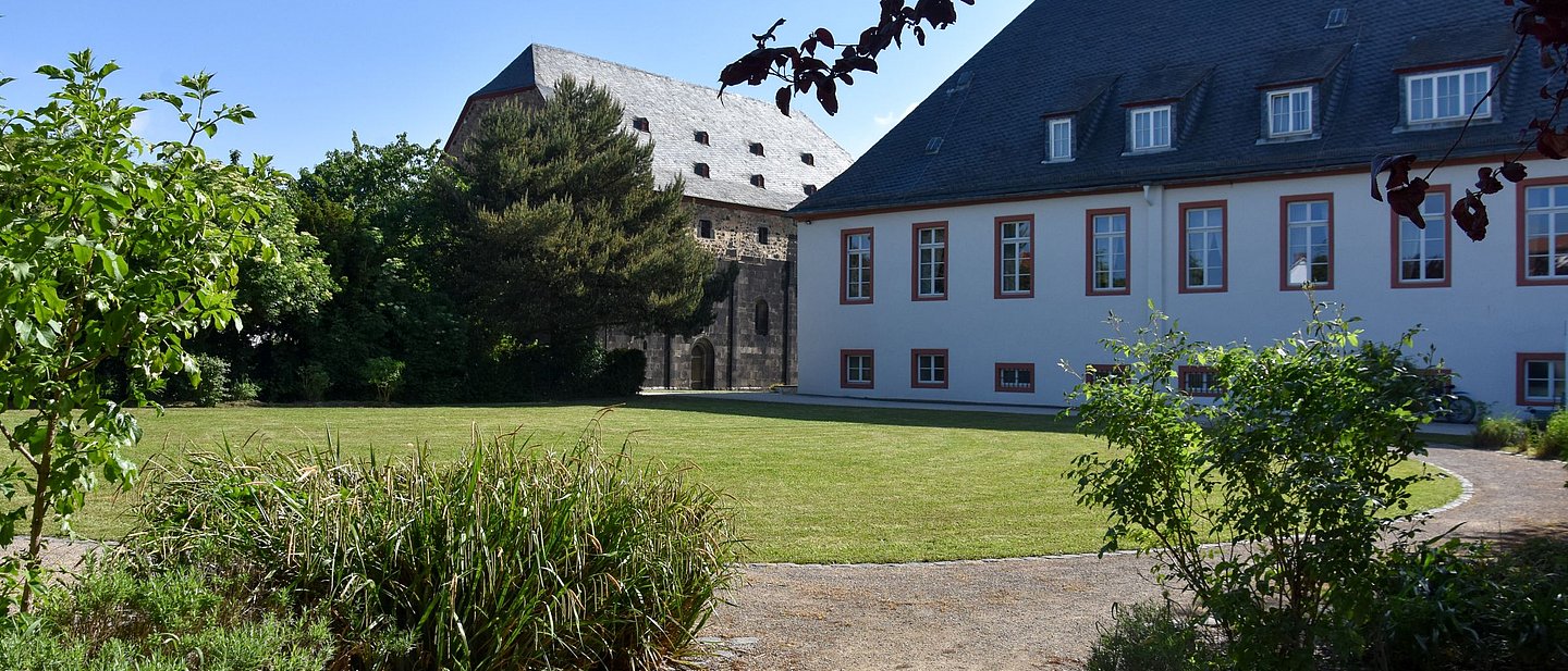 Kirche und Ordenshaus, im Vordergrund Pflanzen und eine grüne Wiese