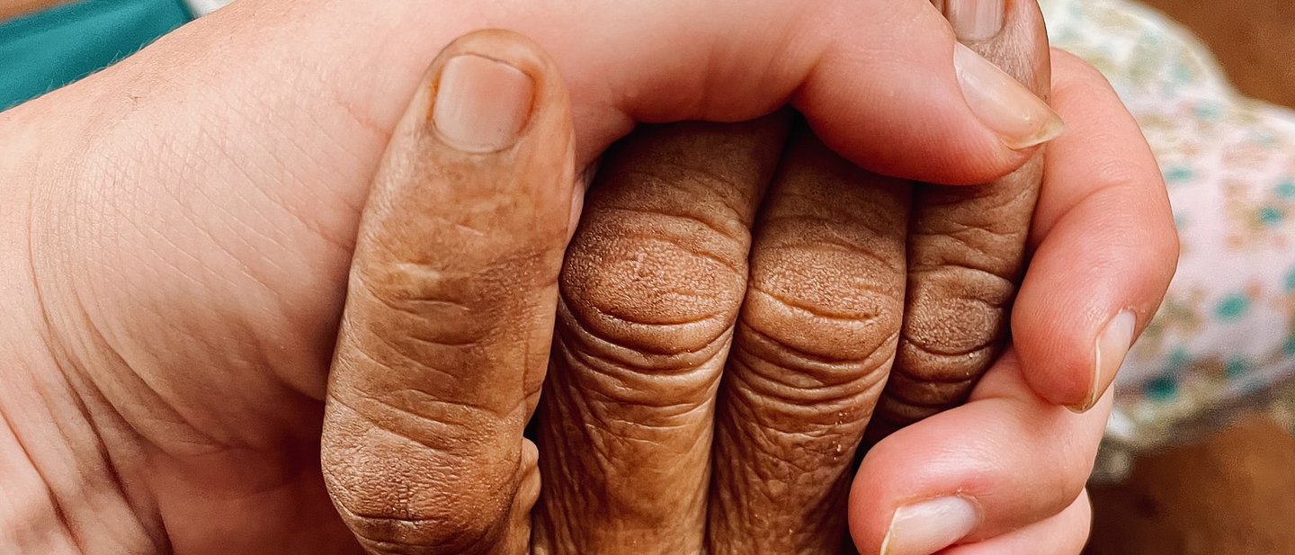 Zwei Hände halten sich, eine mit weißer Haut, eine mit brauner Haut.