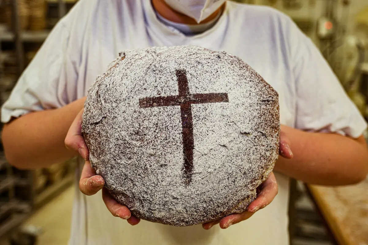 Konfirmand in der Bäckerei Fink in Steinau beim Backen von Brot. Für die Aktion "5000 Brote" wird Brot gebacken, welches auf Spendenbasis verkauft werden und der Hilfsorganisation Brot für die Welt zugute kommen soll. Im Vordergrund ist das Brot mit einem Kreuz, das von einem Konfirmanden in seinen Händen gehalten wird.