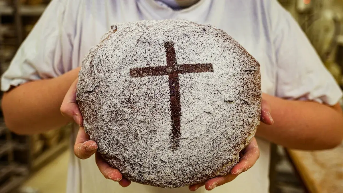 Konfirmand in der Bäckerei Fink in Steinau beim Backen von Brot. Für die Aktion "5000 Brote" wird Brot gebacken, welches auf Spendenbasis verkauft werden und der Hilfsorganisation Brot für die Welt zugute kommen soll. Im Vordergrund ist das Brot mit einem Kreuz, das von einem Konfirmanden in seinen Händen gehalten wird.