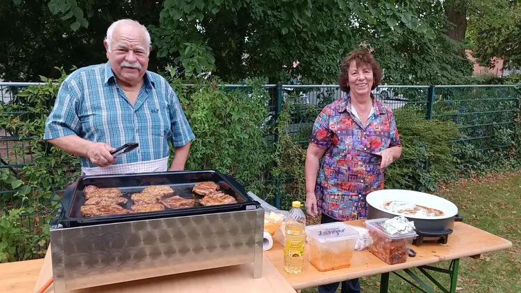 2 Personen stehen am Grill und grillen Steak und Wurst