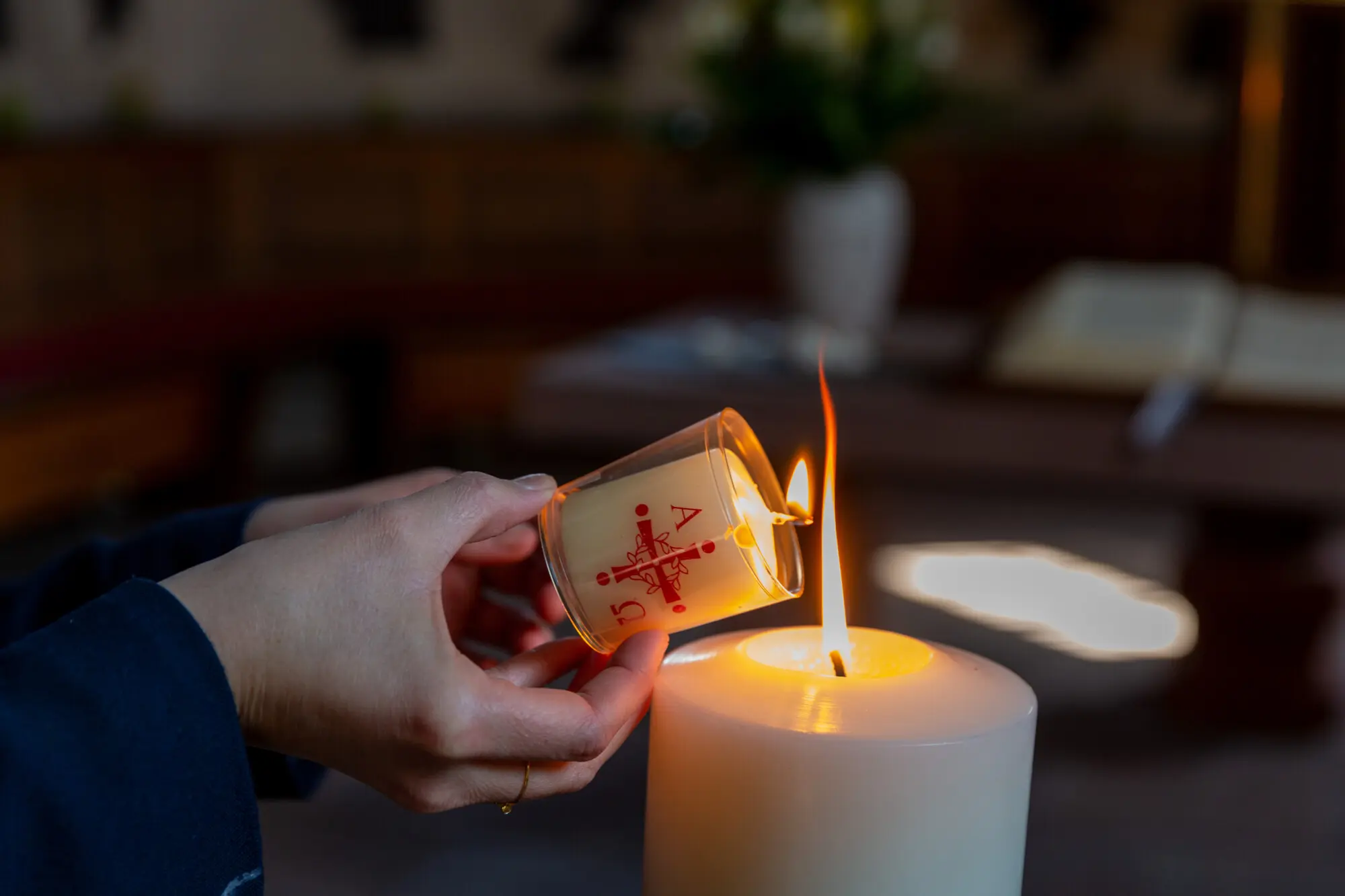 Jemand zündet eine Kerze an der Osterkerze in einer Kirche an.