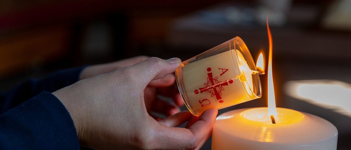 Jemand zündet eine Kerze an der Osterkerze in einer Kirche an.