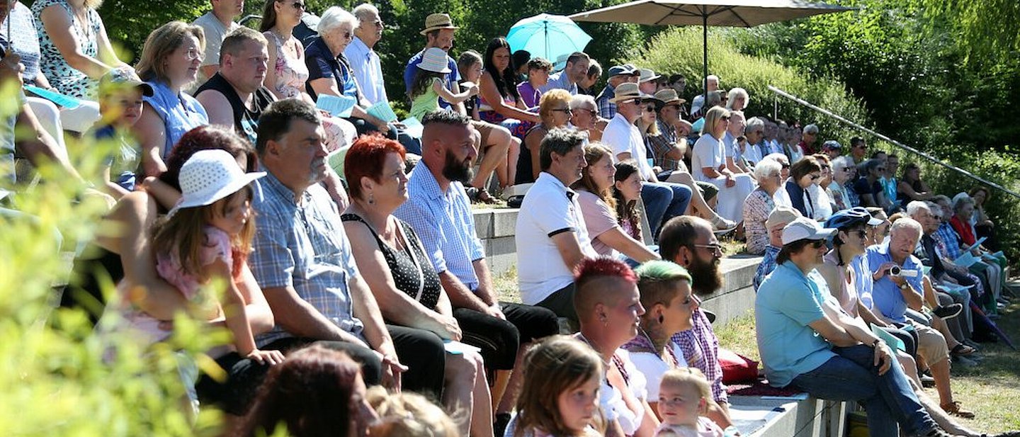 grüne Wiese, graue Steinstufen. Ca 100 Menschen