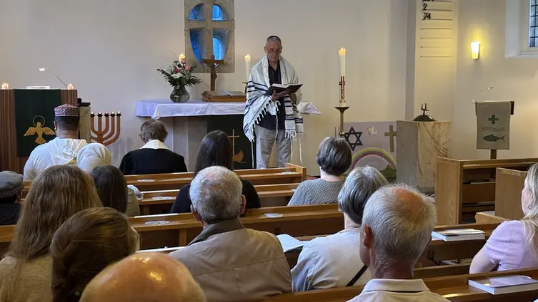 Ein Mann im jüdischen Gebetsmantel spricht zu Gottesdienstbesuchern in einer christlichen Kirche