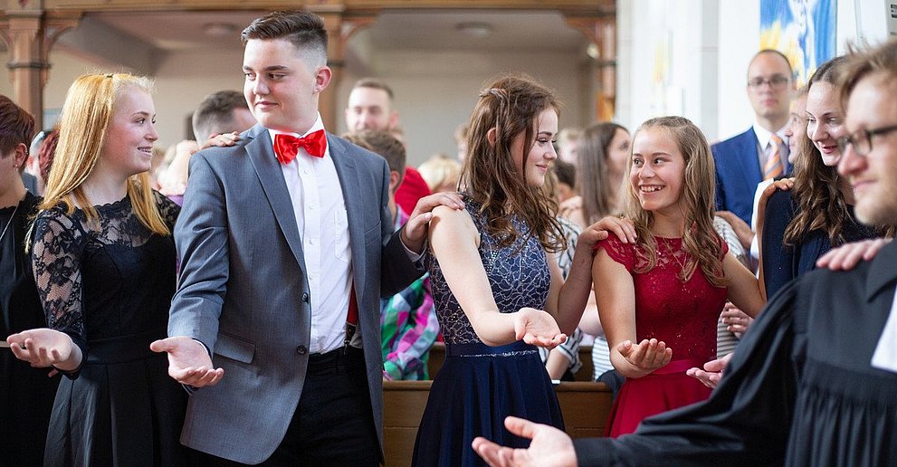 Konfirmandinnen und Konfirmanden reichen sich die Hände beim Gottesdienst  in der Kirche