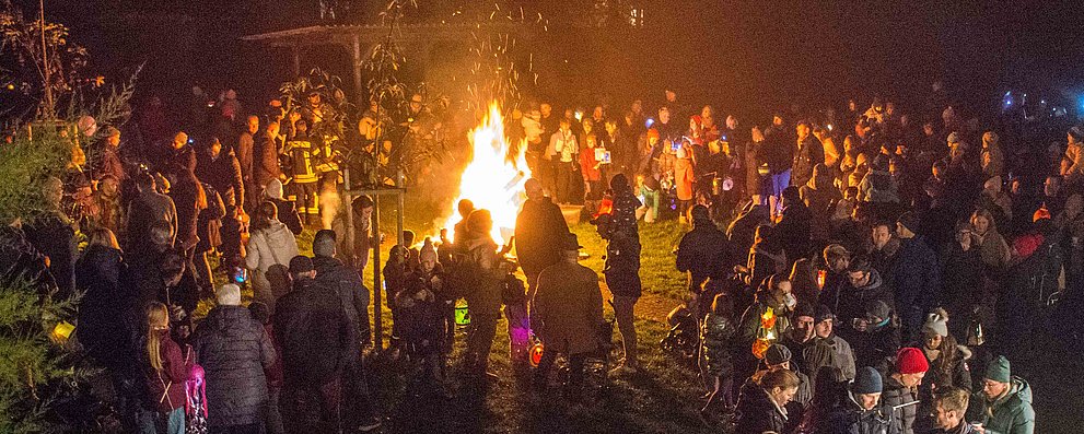 Große Menschenmenge rund um das Martinsfeuer im Kirchgarten der katholischen Kirche Burgholzhausen