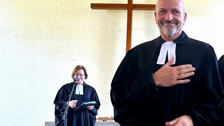 Andreas Lipsch im Talar vor der Kirchenbank hält sich die Hand aufs Herz im Hintergrund die Stellv. KP Scherf auch im Talar 