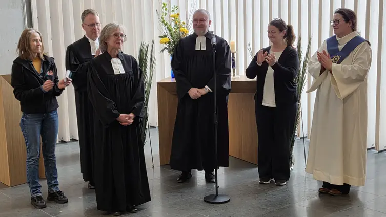 Fünf Menschen stehen im Halbkreis hinter der Pfarrerin und klatschen Beifall