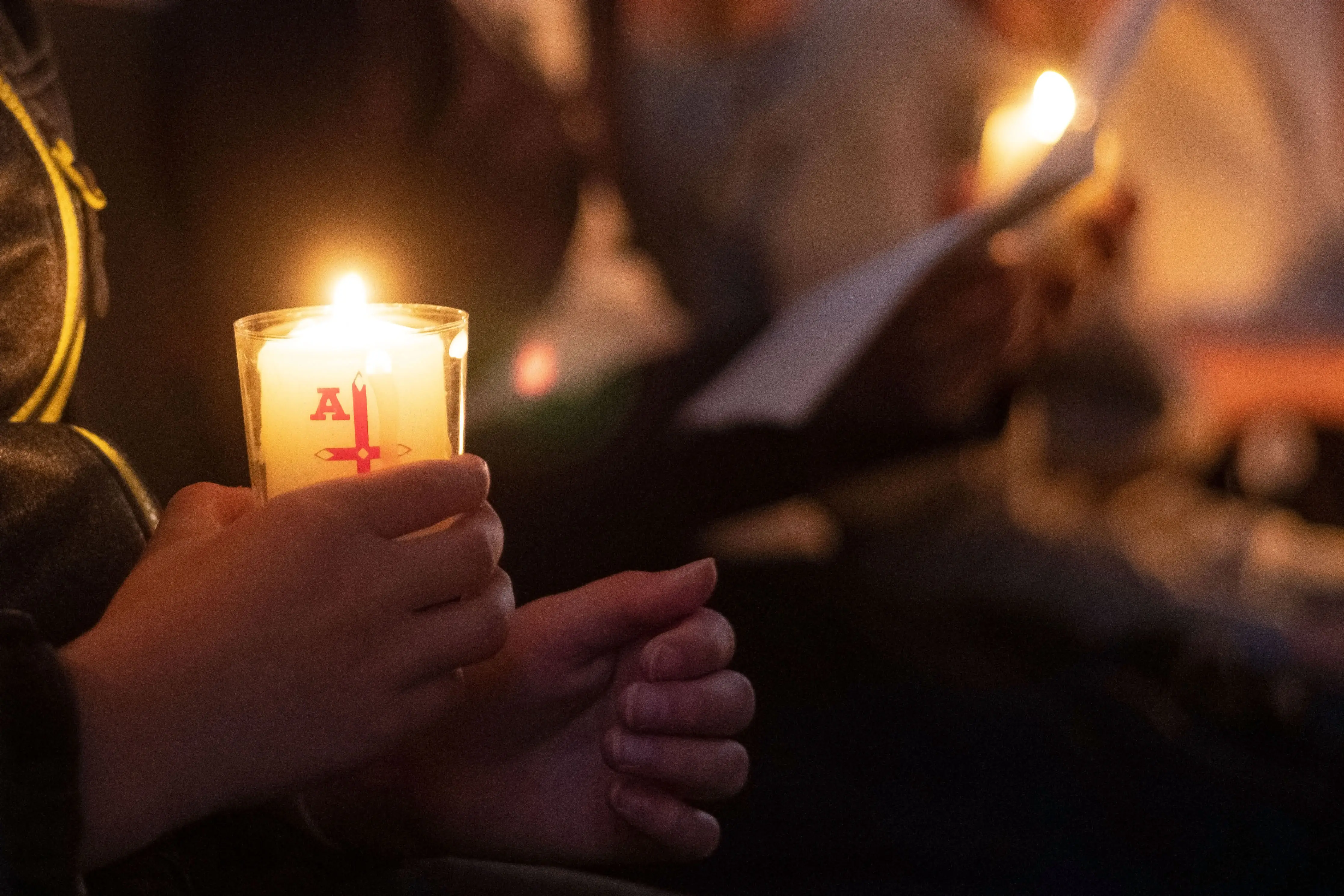 Blick in eine dunkle Kirche, man sieht Hände, die eine Kerze halten 