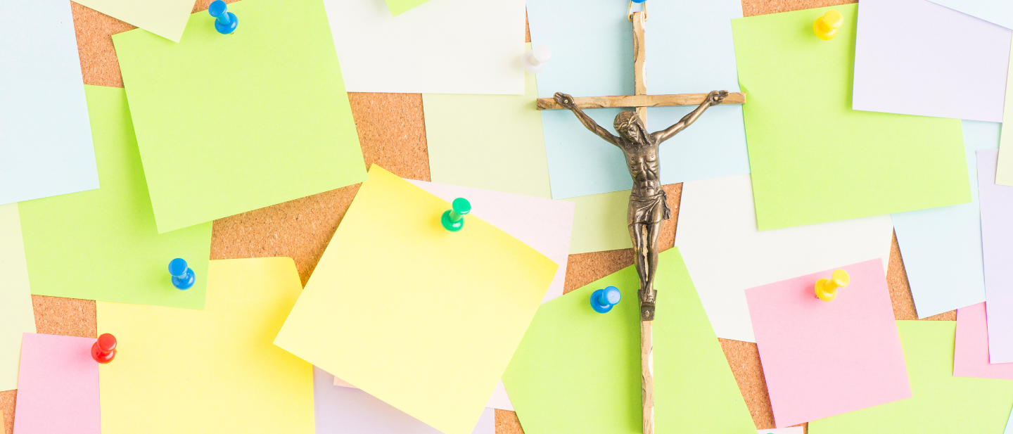 Ein kleines Jesuskreuz hängt an einer Pinwand mit vielen Post-its