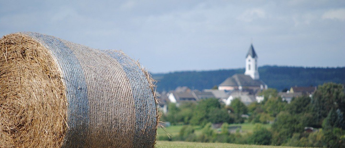 Ein Strohballen auf einem Feld, im Hintergrund eine Kirche.