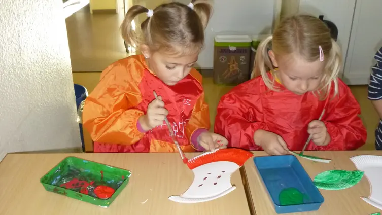 Das Foto zeigt 2 Mädchen im "Haus des Kindes", die aus einem Pappteller einen angebissenen Apfel basteln.