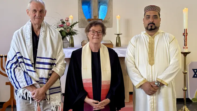 Ein jüdischer Vorbeter, eine evangelische Pfarrerin und ein islamischer Imam stehen in einer Kirche