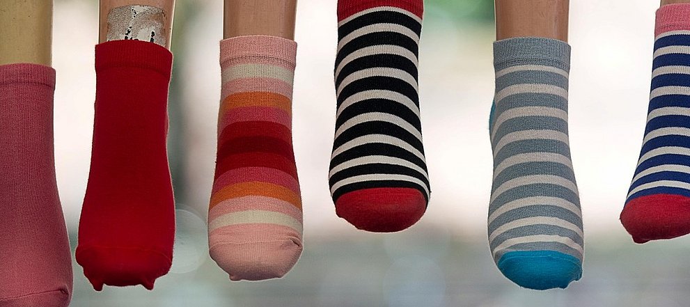 Sechs baumelnde Füße mit verschiedenen, bunten Socken