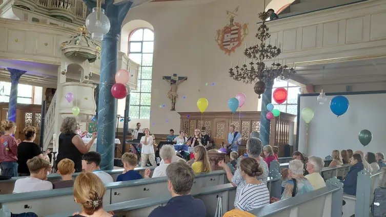 Das Foto zeigt den vollbesetzten und bunt dekorierten Kirchenraum der Sandbacher Kirche mit tanzenden Menschen