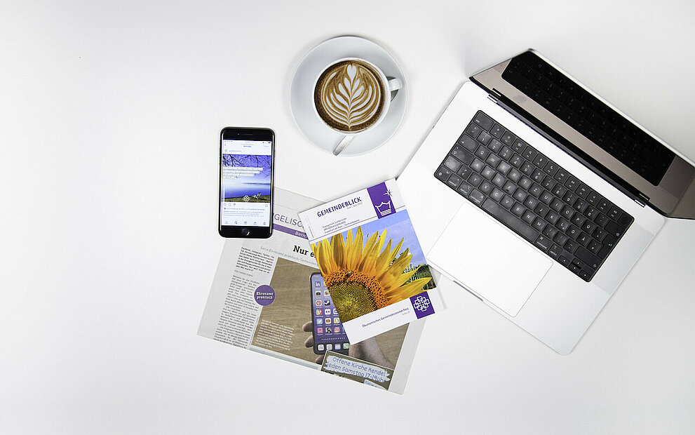 Ein Fundus Flyer, Laptop, Zeitung, Smartphone und eine Tasse Kaffee liegen auf einer weißen Fläche.