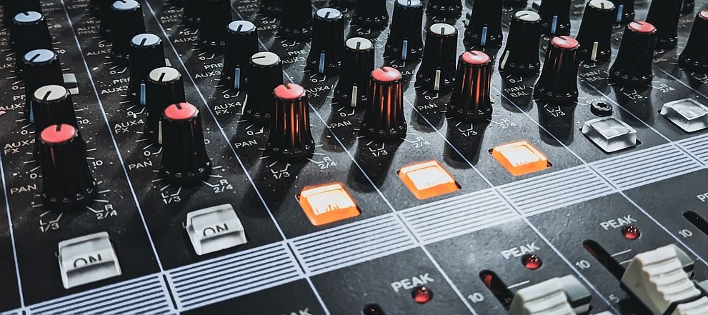 Detailaufnahme eines Audiomischpults mit hervorgehobenen Knöpfen und leuchtenden Lichtern