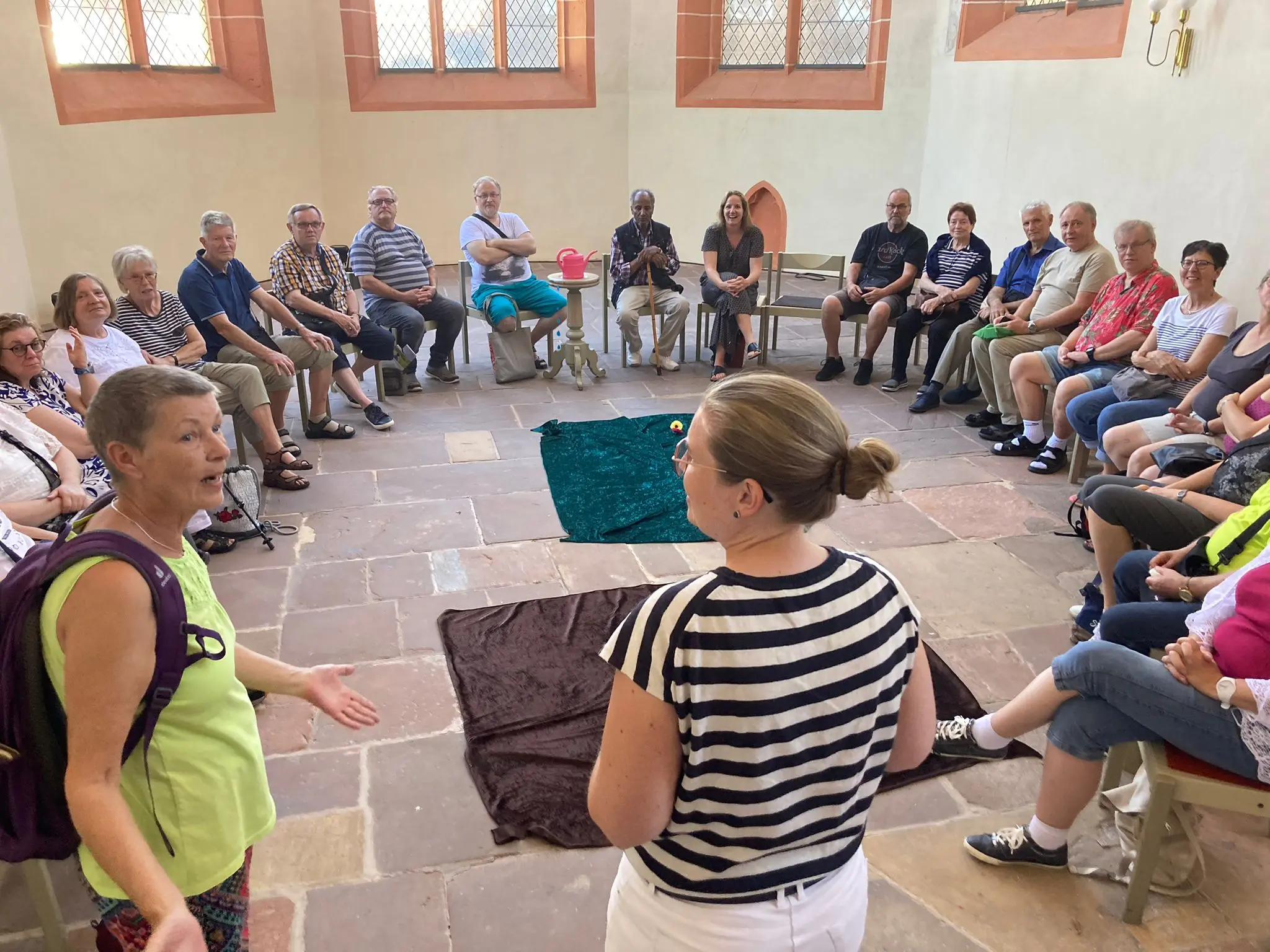 Gruppe von Menschen sitzt in einem großen Kreis in einem hellen Raum mit Kirchenfenstern und unterhält sich.