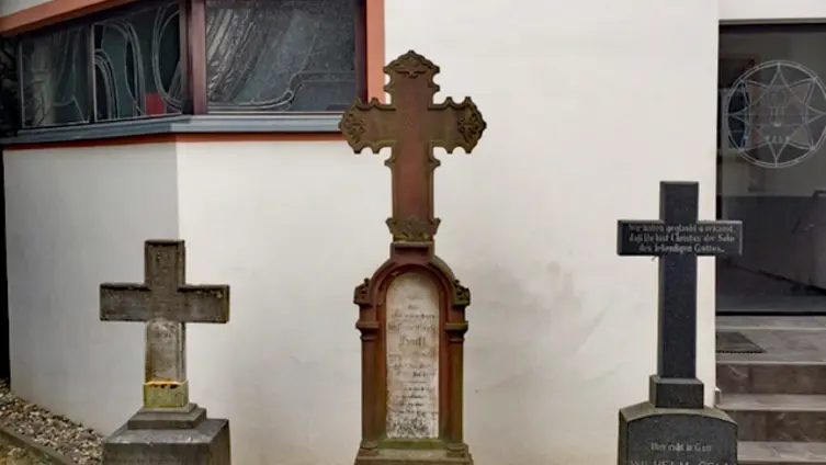 Drei alte Grabmäler mit Steinkreuzen vor dem Sakristei-Anbau. Das mittlere Kreuz ist höher als die äußeren.