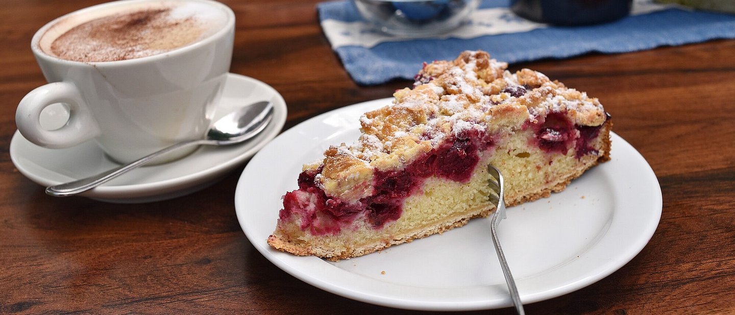 Ein Stück Kirsch-Streuselkuchen und ein Cappuccino.