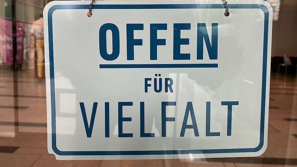 Offen für Vielfalt An der Innenseite eines Schaufensters hängt ein Schild mit der Aufschrift "Offen für Vielfalt" in Großbuchstaben. Die Schrift ist blau auf weißem Grund