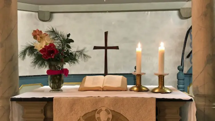 Der von zwei Säulen eingerahmte Sandsteinaltar der evangelischen Kirche Köppern mit weißem Altartuch, zwei Kerzen rechts darauf,  Bibel mit Kreuz dahinter und links ein weihnachtlicher Strauß. Darüber der Herrnhuter Stern.