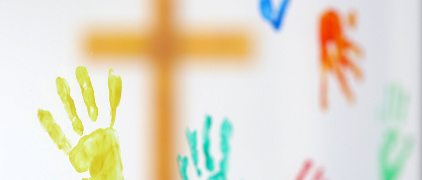 Fenster mit Bunten Handabdrücken, dahinter ein Kreuz