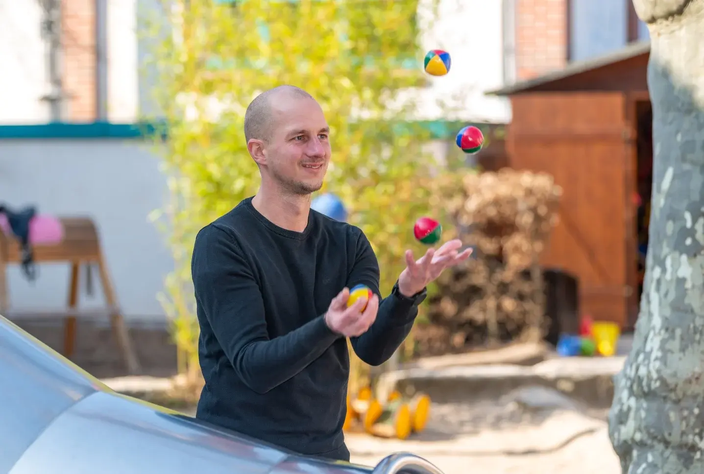 Auf einem Spielplatz neben der Rutsche jongliert ein Mann mit vier bunten Bällen 