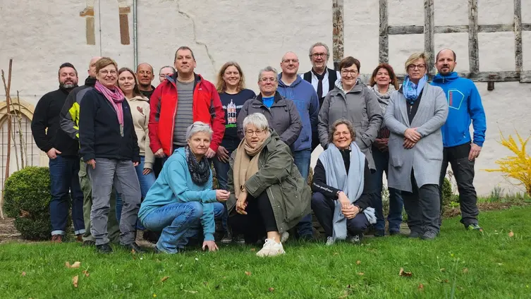 Eine Gruppe von Menschen kniet und steht in zwei Reihen vor einem alten Gemäuer. 