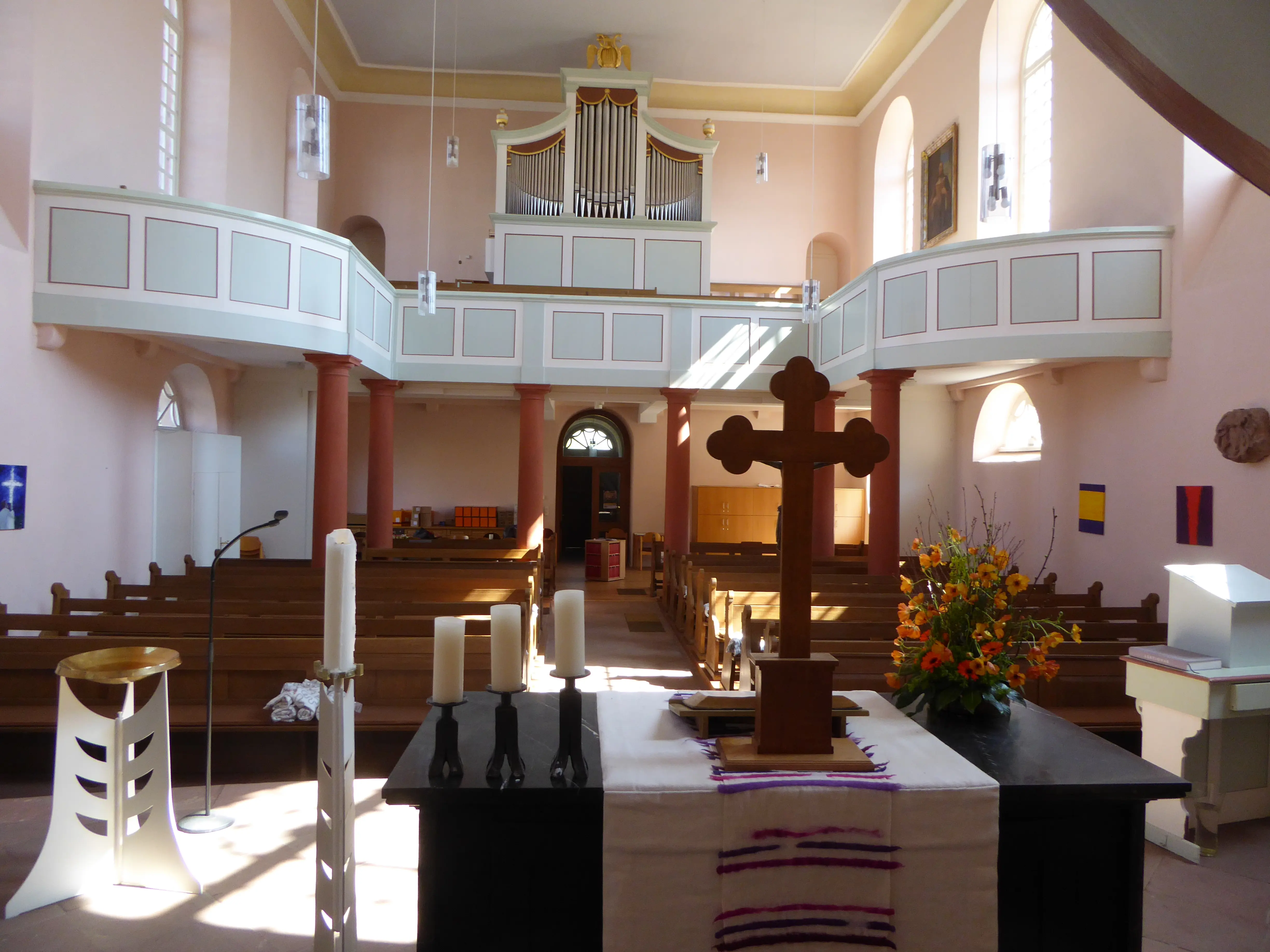 Blick in das Kirchenschiff und auf die Empore mit Orgel, im Vordergrund Altar mit Kreuz, Blumen und Kerzen
