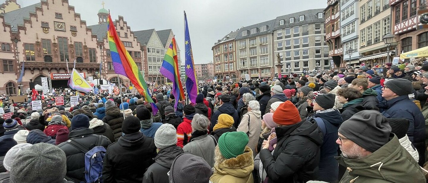 Demo gegen rechts in Frankfurt am Main 2024. Demonstrantinnen und Demonstranten stehen mit Transparenten und Fahnen vor dem Römer in Frankfurt. Es sind Regenbogenfahnen im Bild zu sehen und Transparente.