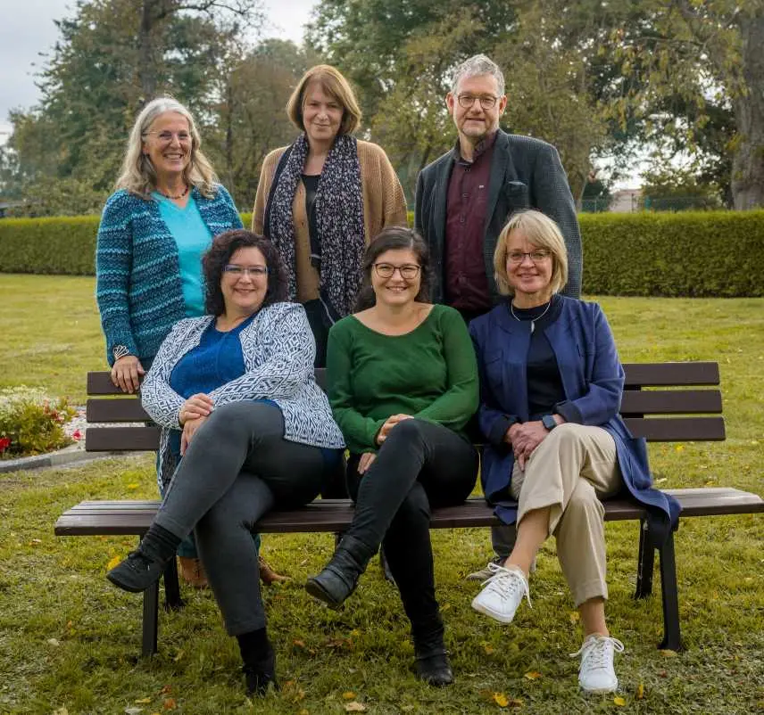 Fünf Frauen und ein Mann, drei auf einer Bank, drei Personen dahinter