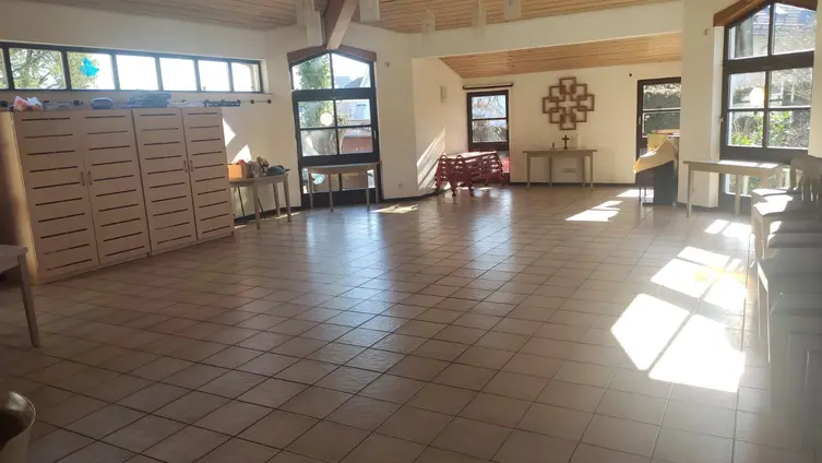 Ein großer, gefließter Raum mit hoher Decke und Fenstern in den Ecken. Auf einer Seite steht ein Schrank, an einer wand hängt ein Facettenkreuz.