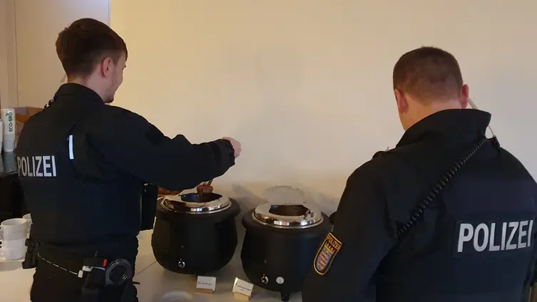 Zwei Polizisten sind von hinten zu sehen. Sie schöpfen Suppe aus einem Warmhaltebehälter.