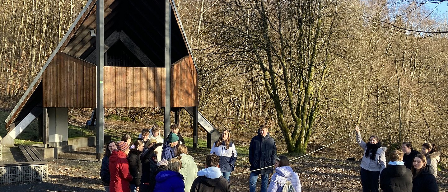Jugendliche spielen draußen vor Herbstlaubbäumen und einer Holzkriche Gruppenspiele