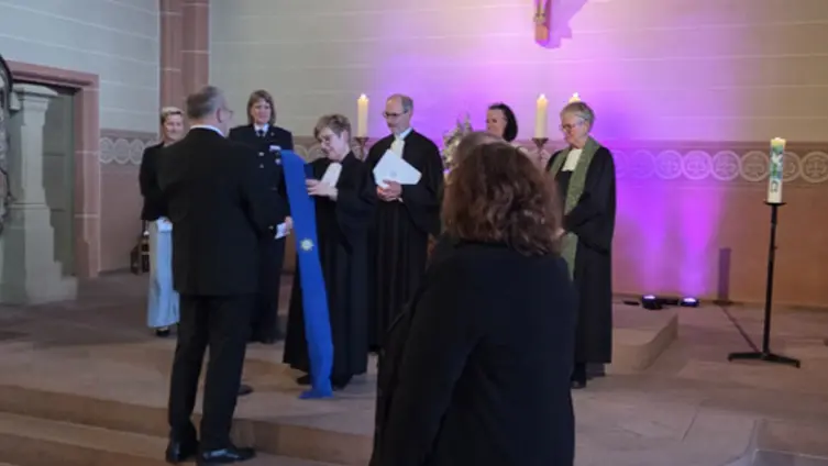 Mehrere Personen stehen vor dem Altar. Die Pfarrerin übergibt eine blaue Stola an den Oberkirchenrat, 